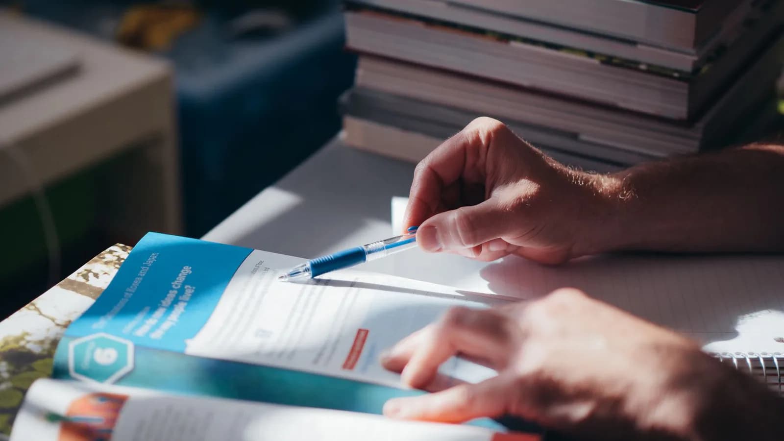 Hands writing on a document beside books and a desk lamp